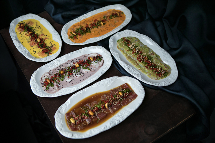 Cinco platos de tiraditos típicos peruanos de diferentes pescados y salsas tradicionales.