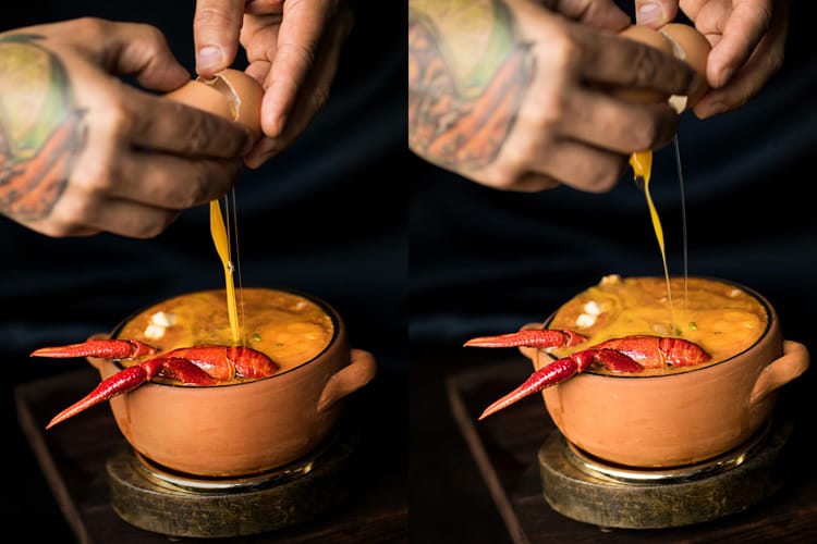 Chef cascando un huevo de gallina sobre bol de chupe peruano de camarón.