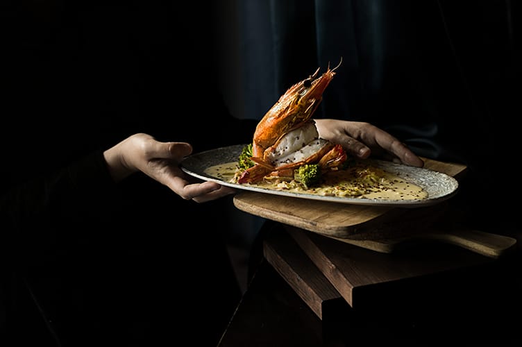 Plato de camarón jumbo abierto sobre salsa de maracuyá peruana y brotes de brócoli frescos.