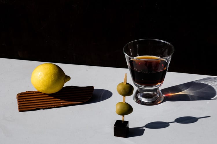 Set fotográfico de un limón, un vermut y una tapa de olivas.