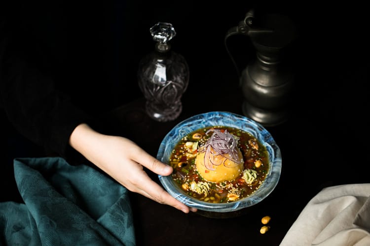 Mano sujetando un plato de causa peruana de atún nikkei con papa amarilla sobre ají triturado. 