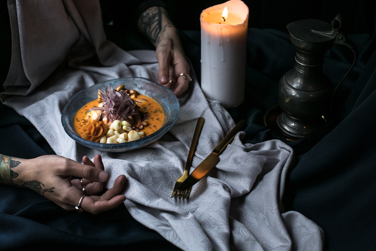 Mano de chef tatuado emplatando con salsa un plato de ceviche peruano de salmón caliente con papa dulce.