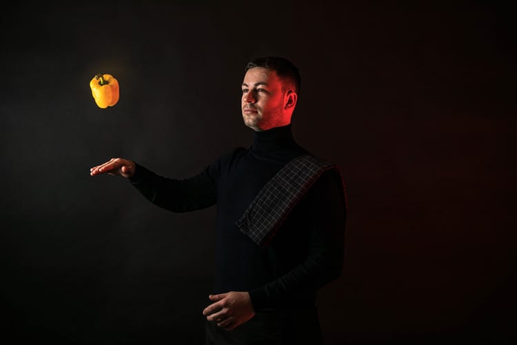 Chef hombre levitando un pimiento amarillo sobre la mano con trapo de cocina en hombro.