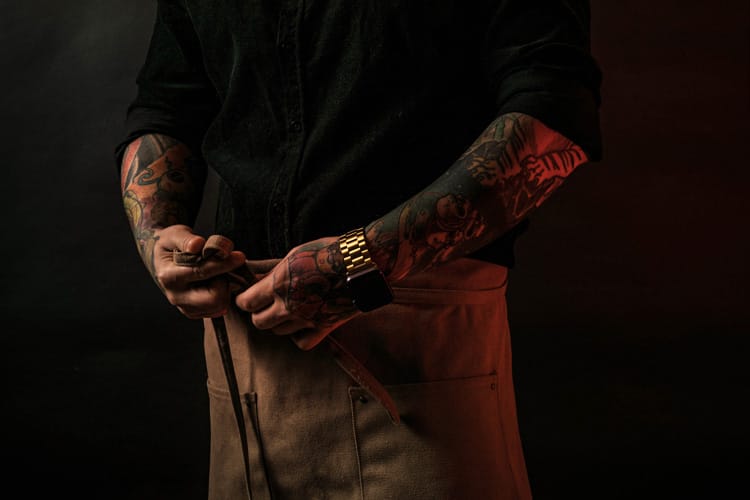 Chef con tatuajes atándose delantal marrón.