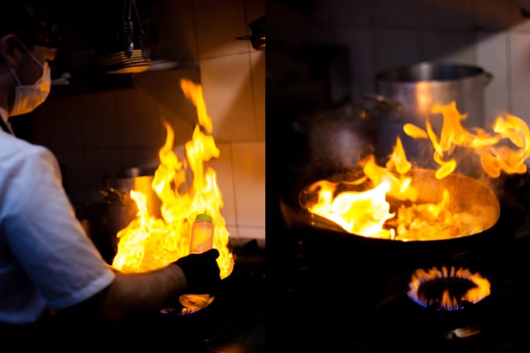 Cocinero flambeando en sartén en llamas echando aceite de oliva.